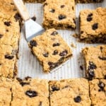 Oatmeal raisin bars cut into squares, with one piece being lifted by a spatula from a baking tray.