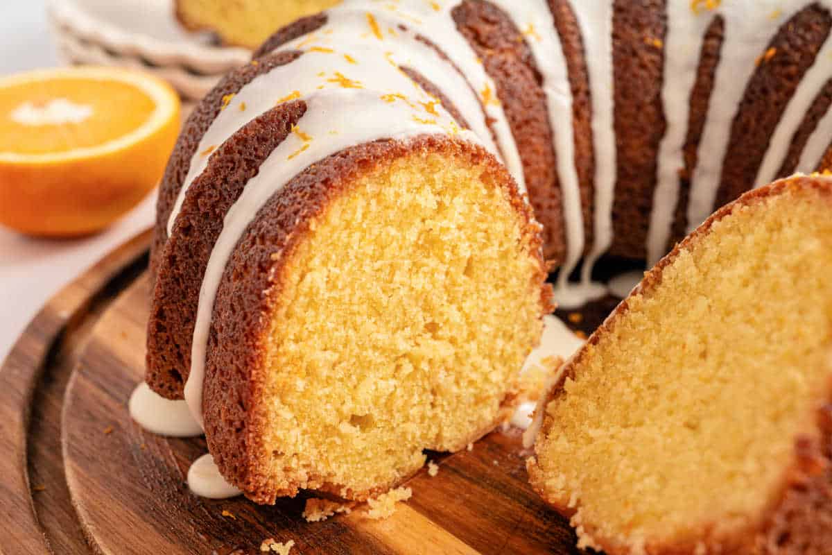Close-up of a sliced orange bundt cake with white glaze, displayed on a wooden board.