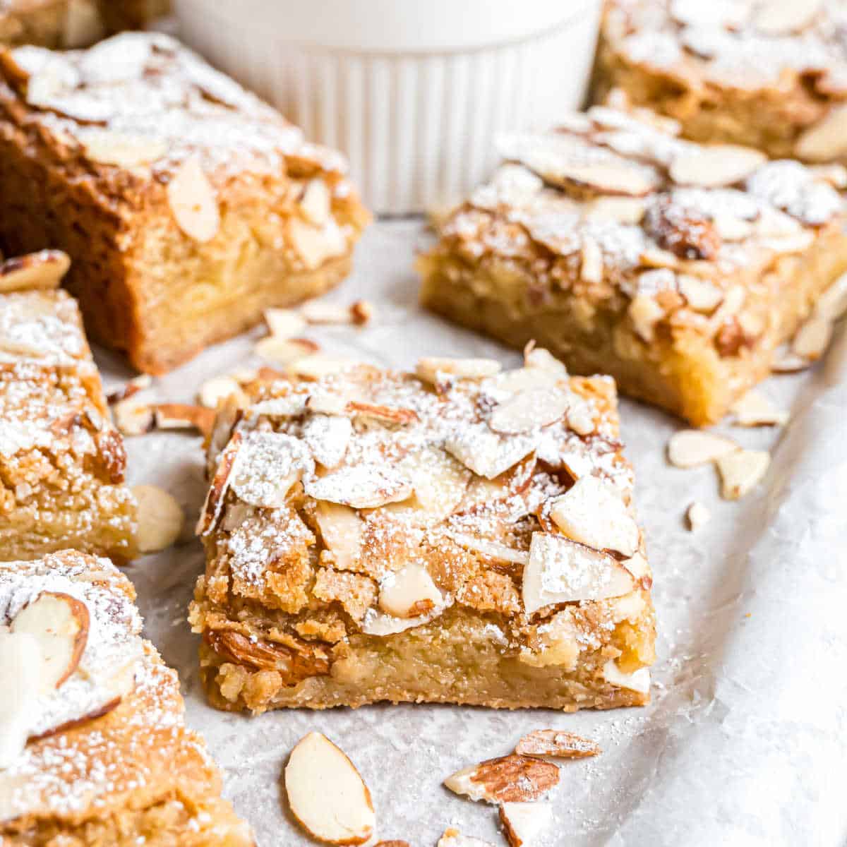 Blondie bars topped with sliced almonds and powdered sugar, arranged on parchment paper.