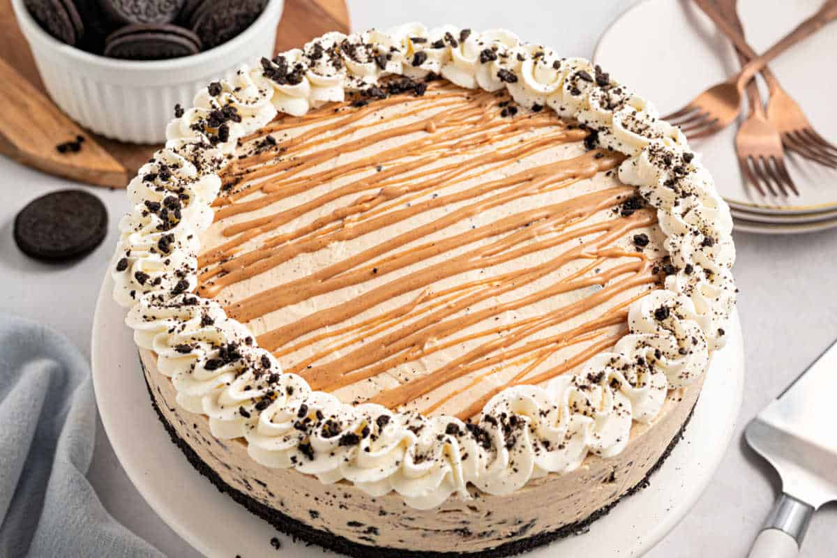 A round cookies and cream cake with whipped cream, cookie crumbles, and caramel drizzle on top.