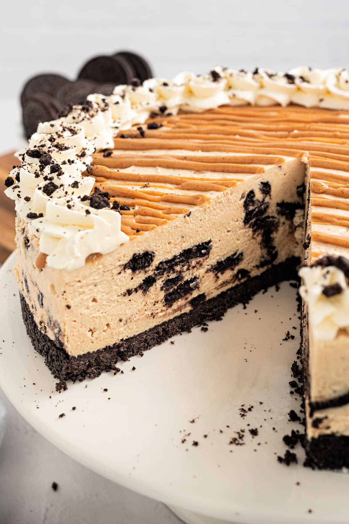 A sliced peanut butter cheesecake with chocolate cookie crust, cookie pieces, and whipped cream on top.