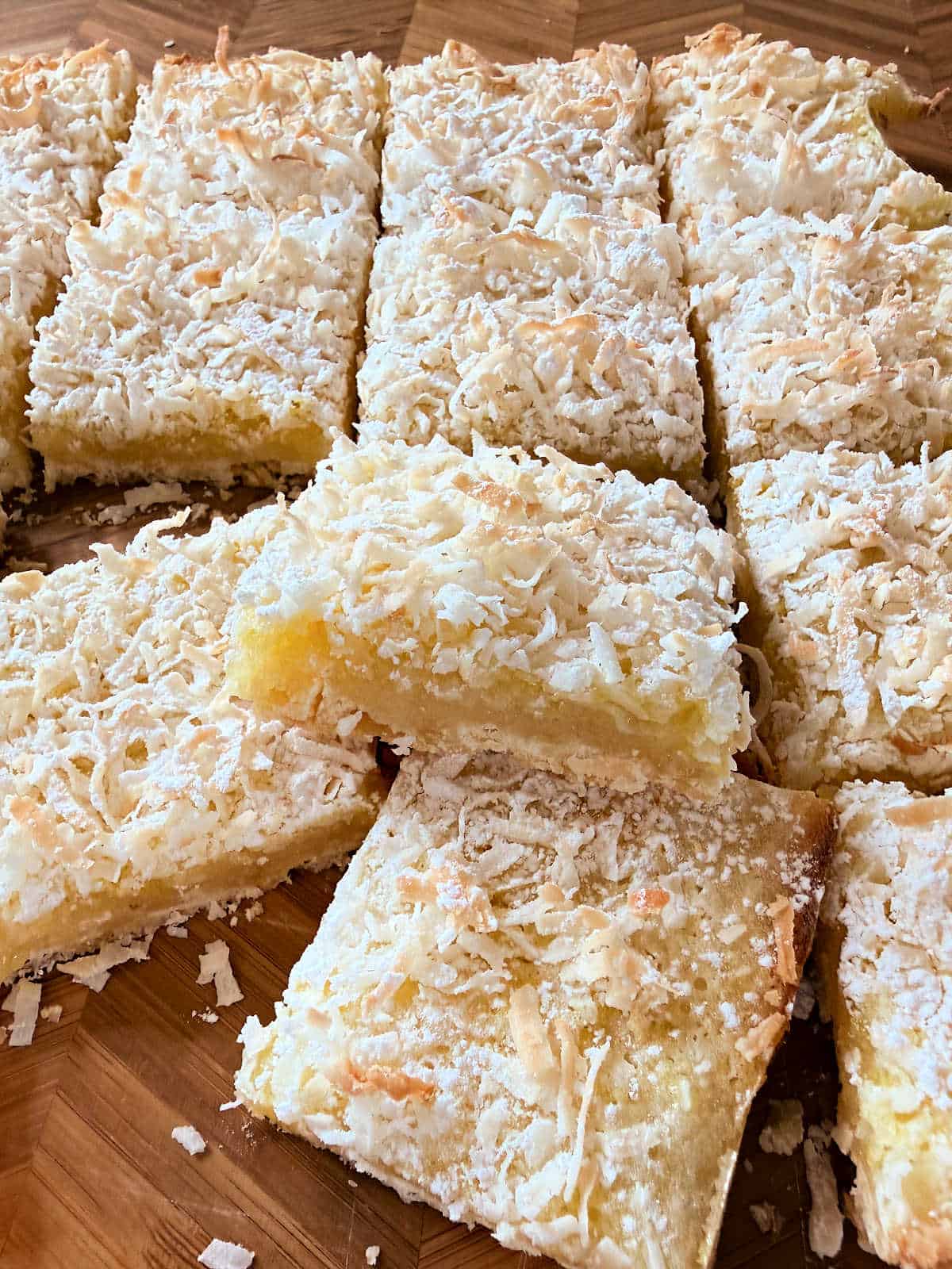 Close-up of coconut-topped lemon bars cut into squares and stacked on a wooden surface.