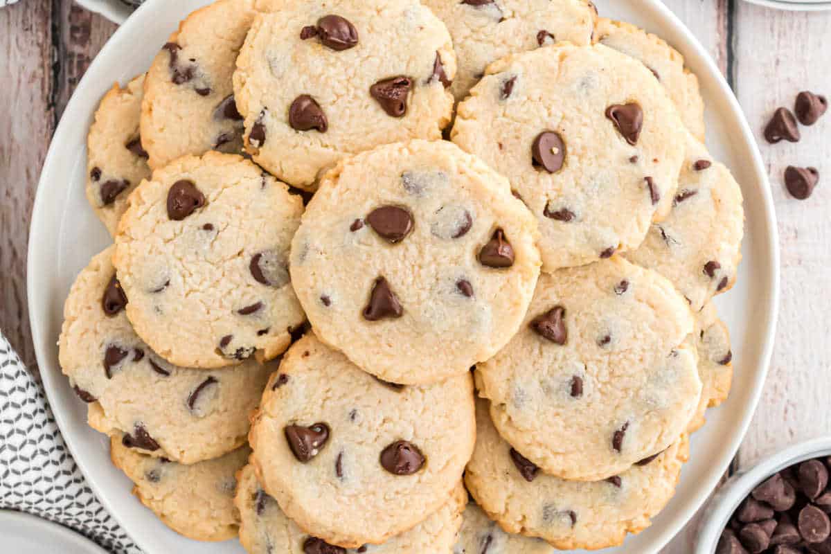 A plate of chocolate chip cookies stacked on top of each other on a white wooden surface.