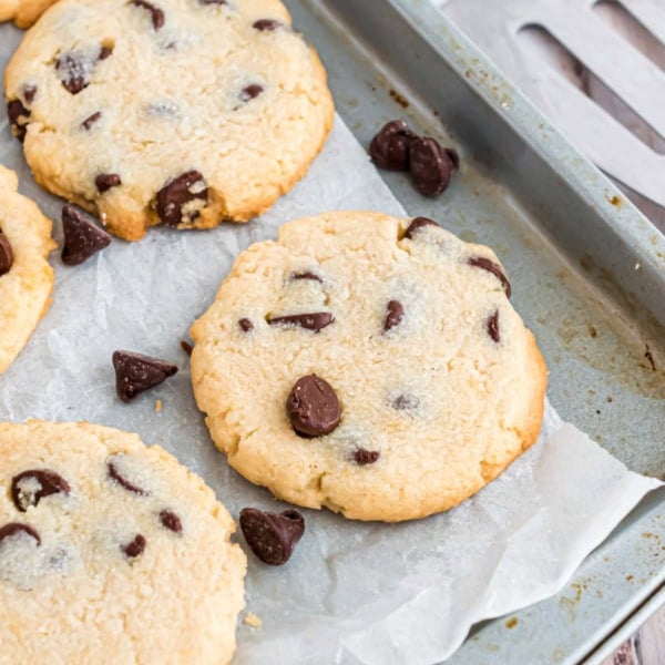 Chocolate chip cookies on a parchment-lined baking sheet, with some chocolate chips scattered around.