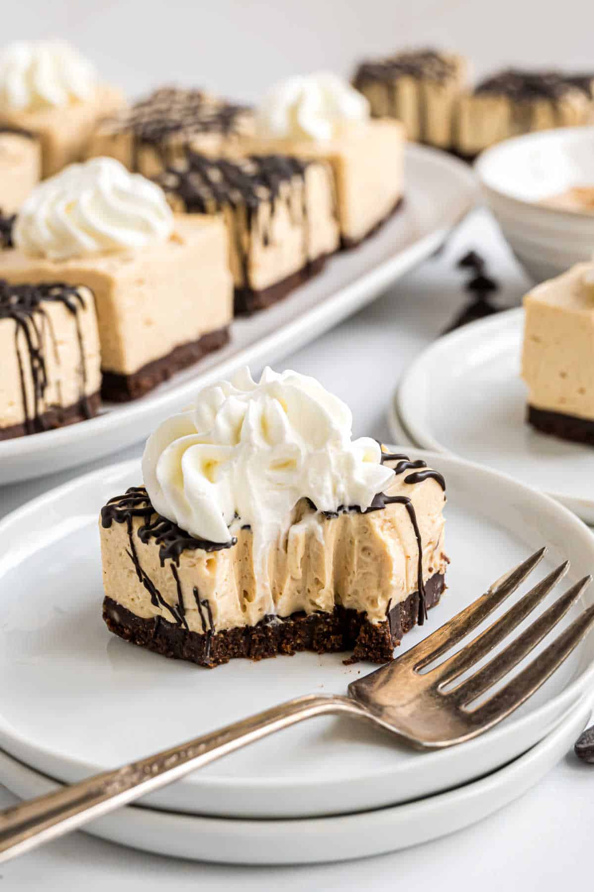 A slice of creamy cheesecake with chocolate drizzle and whipped cream on a plate, with a fork beside it.
