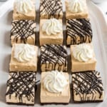 Twelve square dessert bars with a creamy topping, some with chocolate drizzle, arranged neatly on a platter.