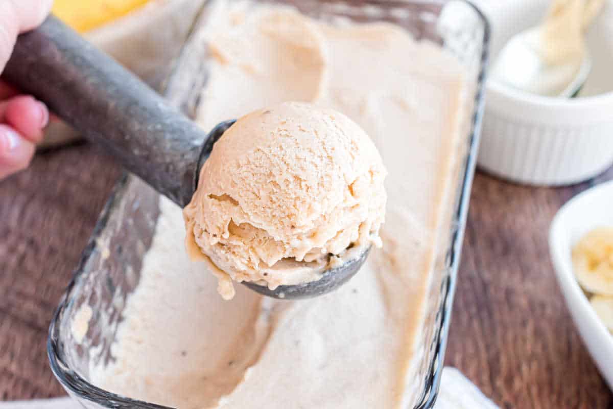 A hand scoops creamy ice cream from a glass dish using a metal ice cream scooper.