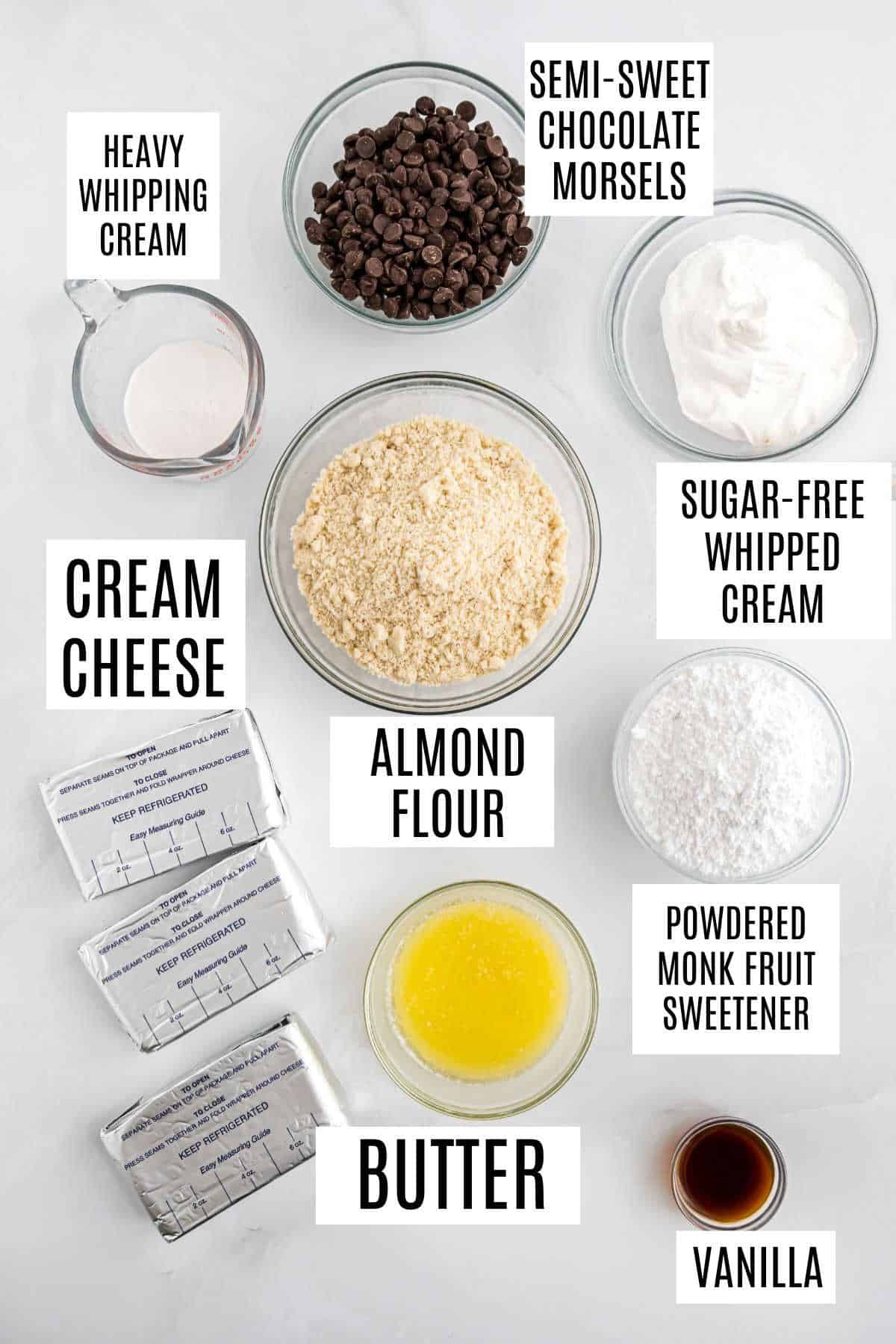 Top view of labeled baking ingredients in bowls: cream cheese, chocolate chips, almond flour, butter, and sweeteners.