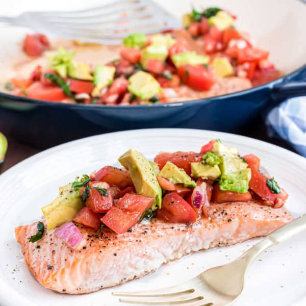Baked salmon fillet topped with avocado and tomato salsa on a white plate with a fork.