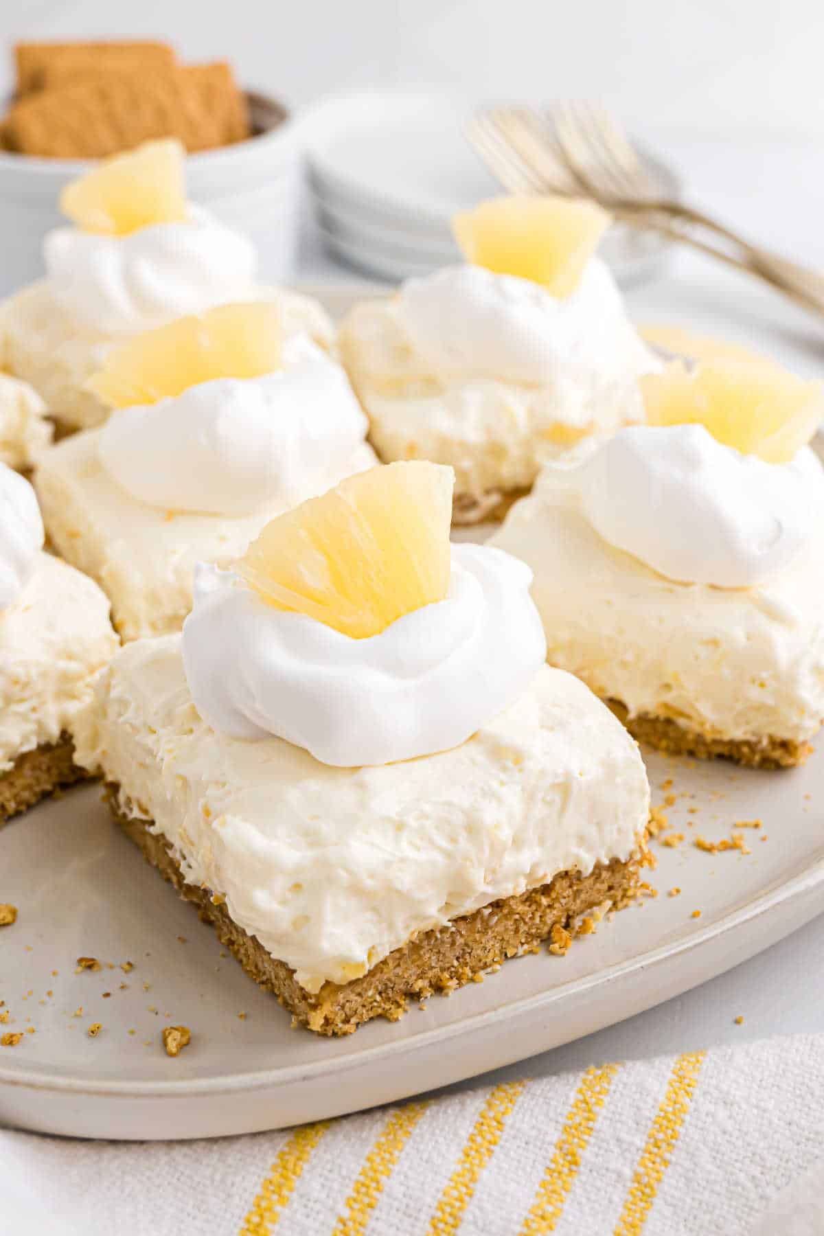 No-bake pineapple cheesecake bars topped with whipped cream and pineapple pieces on a plate.