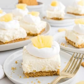 A creamy pineapple dessert bar with whipped topping and pineapple pieces on a plate with a fork.