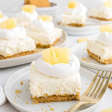 A creamy pineapple dessert bar with whipped topping and pineapple pieces on a plate with a fork.