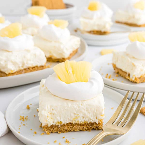 A creamy pineapple dessert bar with whipped topping and pineapple pieces on a plate with a fork.