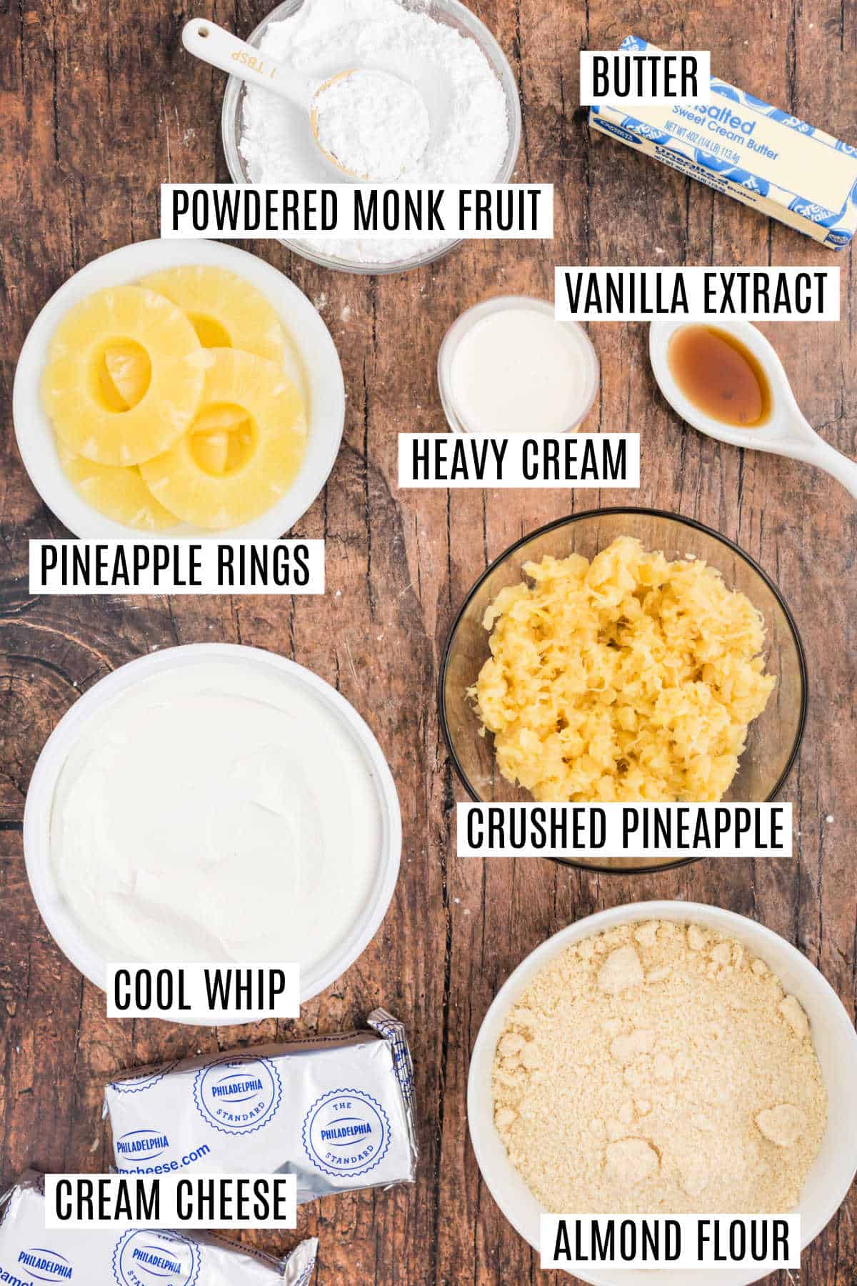 Ingredients for a dessert on a table: pineapple, cream cheese, almond flour, cool whip, butter, and more, all labeled.