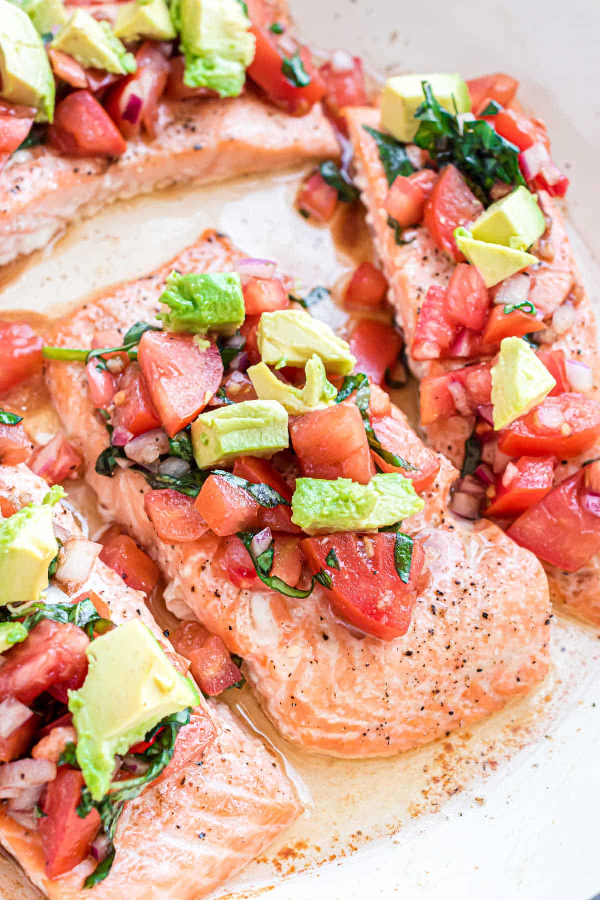 Salmon fillets topped with diced tomatoes, avocado, onions, and herbs on a white plate.