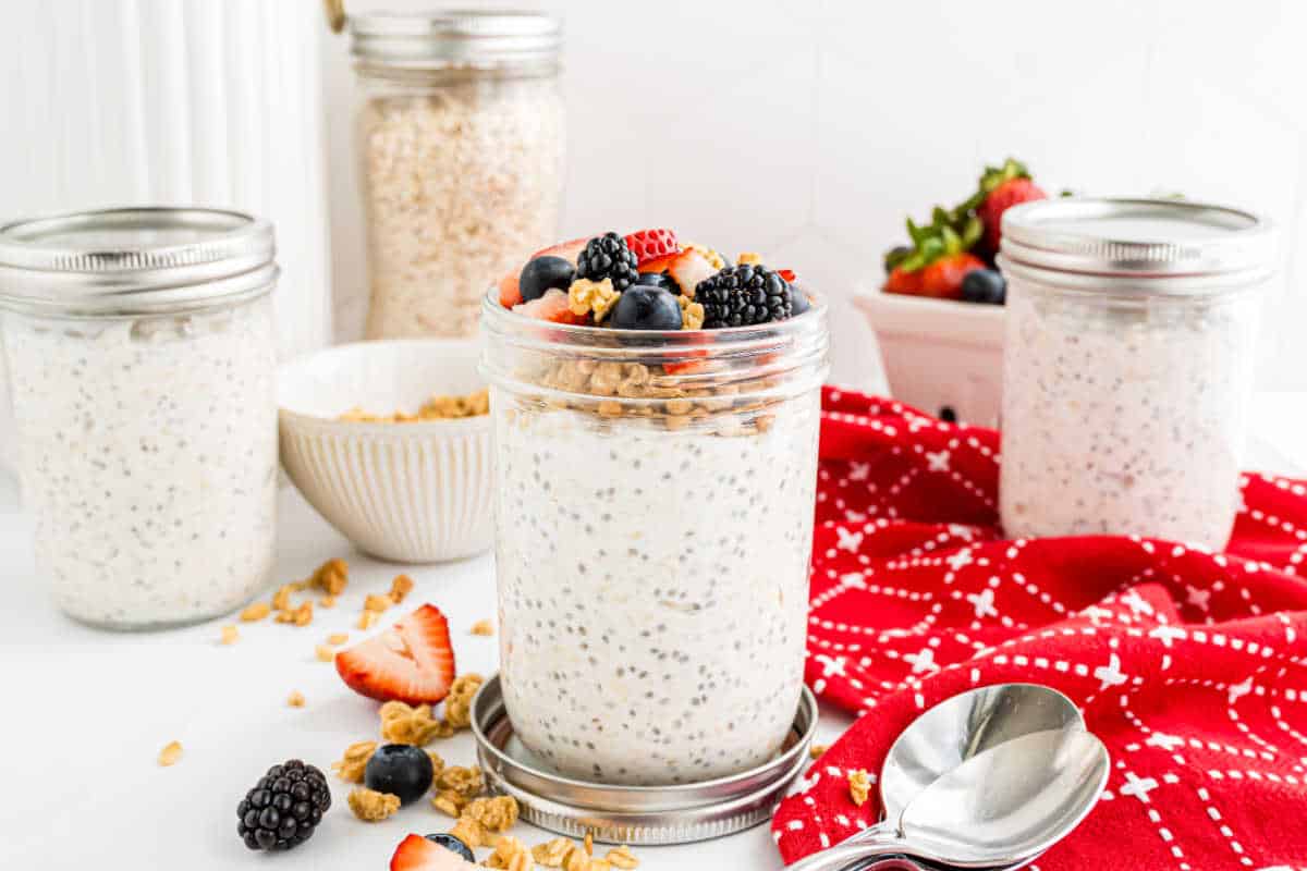 Jar of overnight oats topped with berries and granola, surrounded by fruit, oats, and a red napkin.