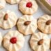 Round amaretti cookies topped with whole almonds or red cherries rest on parchment paper.