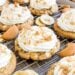 Cookies topped with whipped cream and crumbled wafers on a cooling rack.