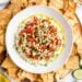 A bowl of whipped feta dip topped with tomatoes, pine nuts, and herbs, surrounded by pita chips.