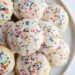 Italian ricotta cookies stacked on plate with colorful sprinkles.