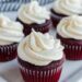 Red velvet cupcakes topped with cream cheese frosting on a plate.