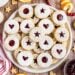 Large white serving platter with linzer cookies stacked on top.